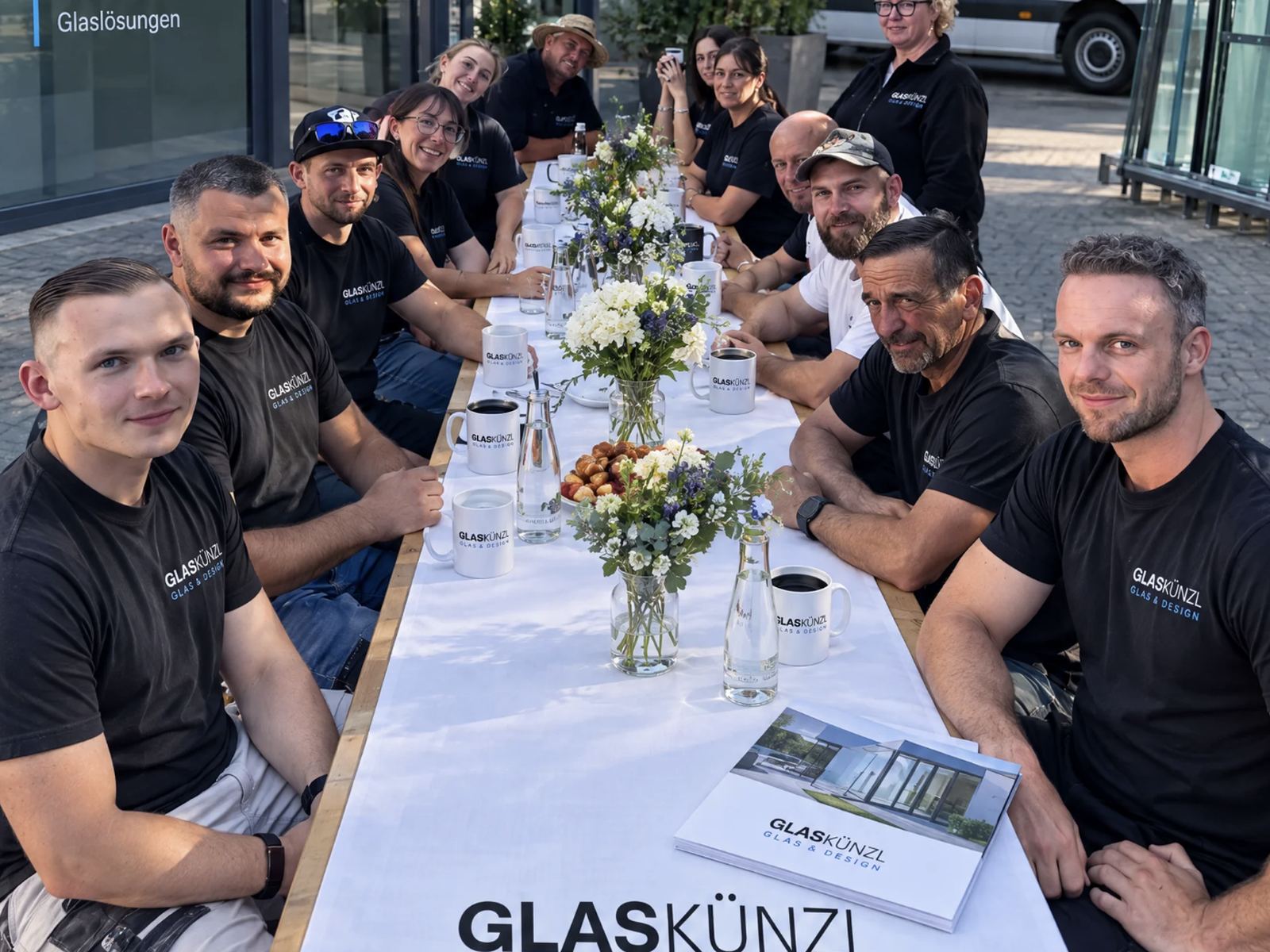 Das Team von GLAS KÜNZL an einer langen Tafel vor dem Firmensitz
